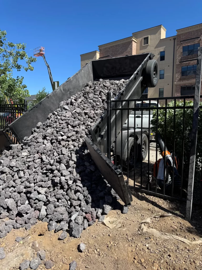 Ponderosa Pathways crew delivering gravel to a Flagstaff dog park using a dump trailer, with the trailer raised and rock being unloaded into the fenced area.