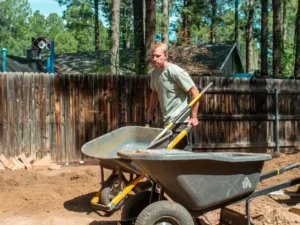 Ponderosa Pathways crew member moving soil amendment with a wheelbarrow during a landscaping job in Flagstaff, Arizona
