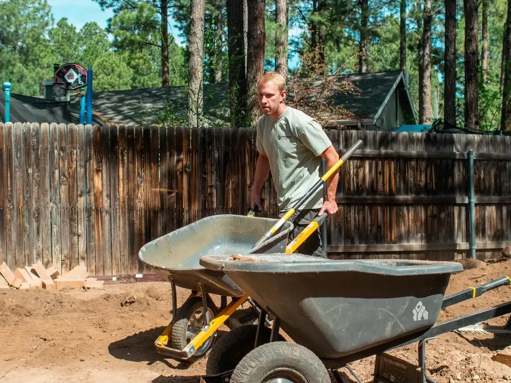 Ponderosa Pathways crew member moving soil amendment with a wheelbarrow during a landscaping job in Flagstaff, Arizona